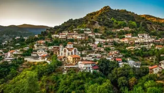 Traditional village on Troodos Mountain with colorful houses and a prominent Orthodox church surrounded by lush green hills at sunset.
