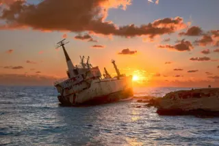 Sunset view of the Edro III shipwreck near the coast of Paphos, Cyprus, with vibrant orange skies and shimmering sea waters.