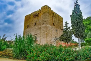 Historic Kolossi Castle surrounded by greenery and flowers near Paphos, Cyprus, under a cloudy sky.