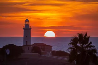 Sunset view of the Paphos Lighthouse with the sun setting over the Mediterranean Sea in Cyprus.