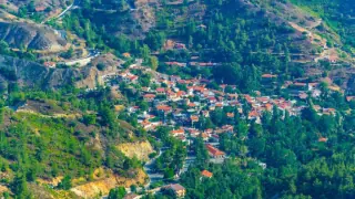 A picturesque mountain village in Cyprus with red-roofed houses nestled among lush green hills and winding roads.