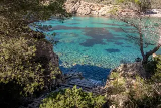A secluded cove with crystal-clear turquoise waters, surrounded by rocky cliffs and lush greenery in Paphos, Cyprus.