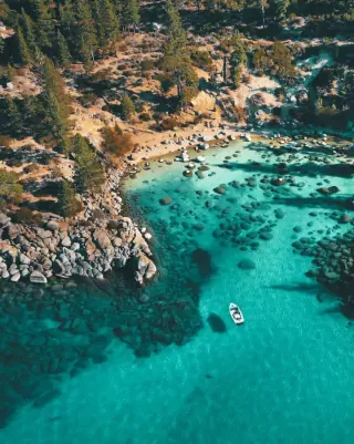 Aerial view of a secluded turquoise bay with a small boat floating in the crystal-clear waters, surrounded by rocky cliffs and lush greenery in Paphos, Cyprus.